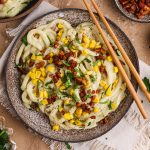 Udon Carbonara in a bowl topped with pecan bacon, corn, and parsley