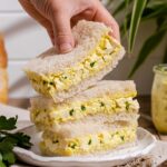 A stack of japanese egg salad sandwiches with a hand going in to grab one half of a sandwich.