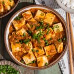 Mapo tofu served in a speckled bowl and garnished with green onions.