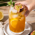 Passion fruit tea is served in a tall glass with a hand coming in to pick the drink up.