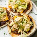 Close up shot of big mac tacos on a white speckled plate with toppings and sauce.
